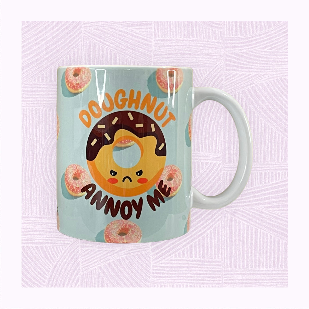 Ceramic mug with a blue background and pink doughnuts, and an angry looking doughnut character with the phrase ‘Doughnut Annoy Me’.