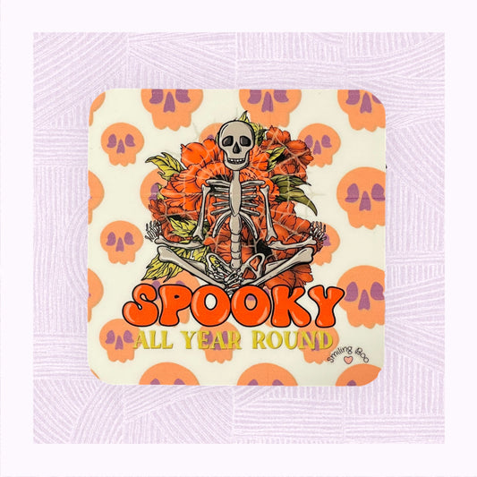 Square coaster with a background of raining skulls, a large skeleton in the foreground with the phrase ‘Spooky All Year Round’ underneath it.