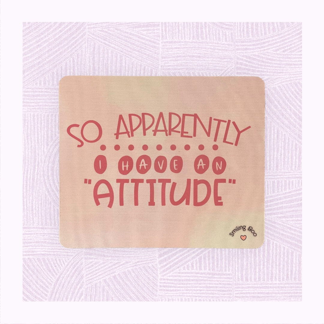 Rectangle mouse mat with a pastel pink background and the phrase ‘Apparently I have an Attitude’ in bubble font.
