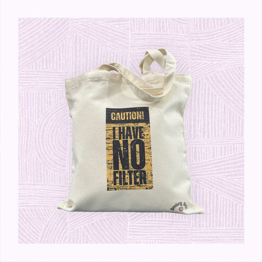 Canvas tote bag with a yellow and black distressed background, with the phrase ‘Caution! I Have No Filter’.