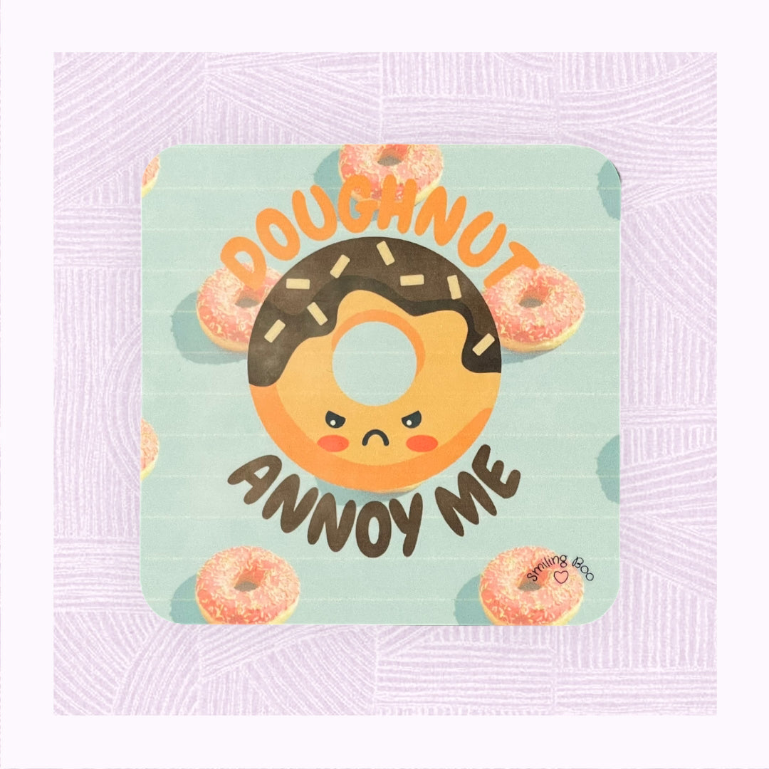 Square coaster with a blue background and pink doughnuts, and an angry looking doughnut character with the phrase ‘Doughnut Annoy Me’.