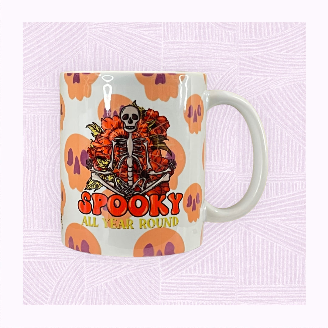 Ceramic mug with a background of raining skulls, a large skeleton in the foreground with the phrase ‘Spooky All Year Round’ underneath it.