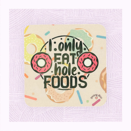 Square coaster with printed background of raining doughnuts, and the phrase ‘I only eat hole foods’ with a pink doughnut either side.