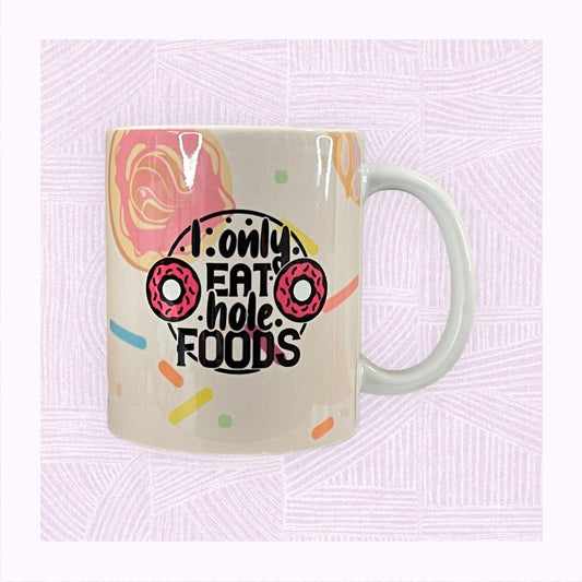 Ceramic mug with printed background of raining doughnuts, and the phrase ‘I only eat hole foods’ with a pink doughnut either side.