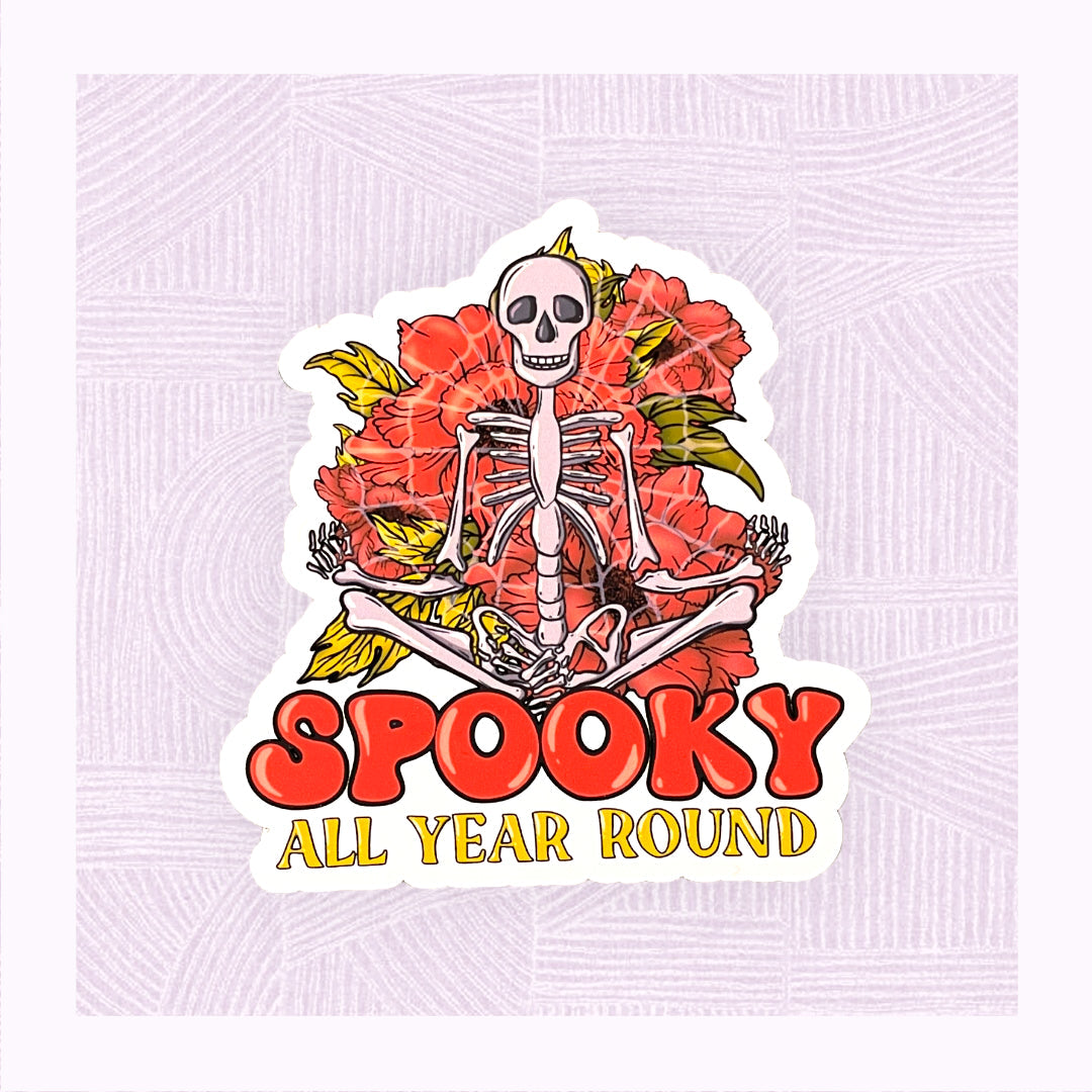 Die cut sticker with a large skeleton in the foreground with the phrase ‘Spooky All Year Round’ underneath it.