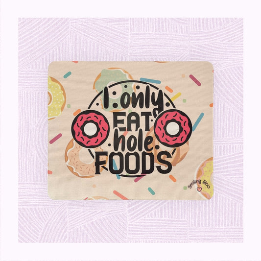Rectangle mouse mat with printed background of raining doughnuts, and the phrase ‘I only eat hole foods’ with a pink doughnut either side.