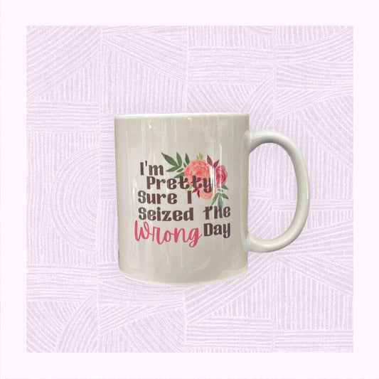 Ceramic mug with a pastel pink/peach watercolour background with the phrase ‘I’m pretty sure I seized the wrong day’ and floral arrangement